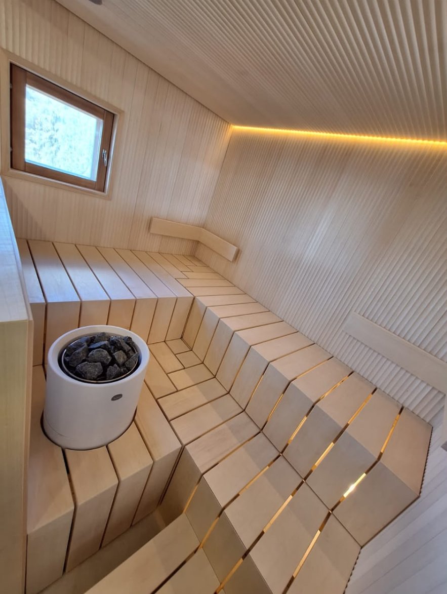 Vaalea sauna porrastetuilla lauteilla, LED-valaistuksella ja pyöreällä kiukaalla